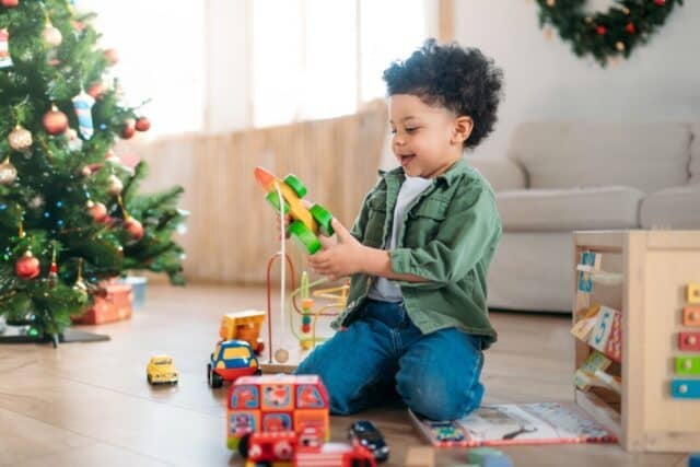 African american curly haired boy child on floor playing with christmas presents near tree in light room