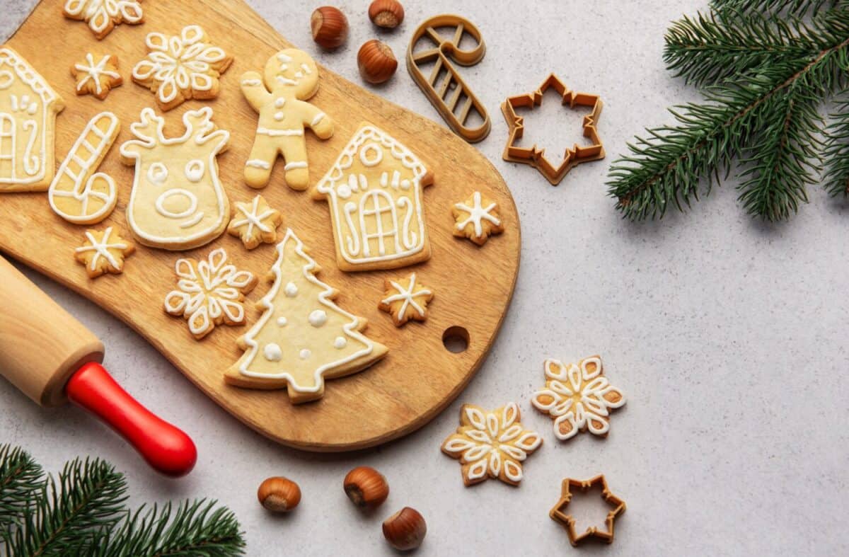Christmas cookies decorated with icing displayed on a wooden board, along with fir branches and hazelnuts, creating a festive holiday scene