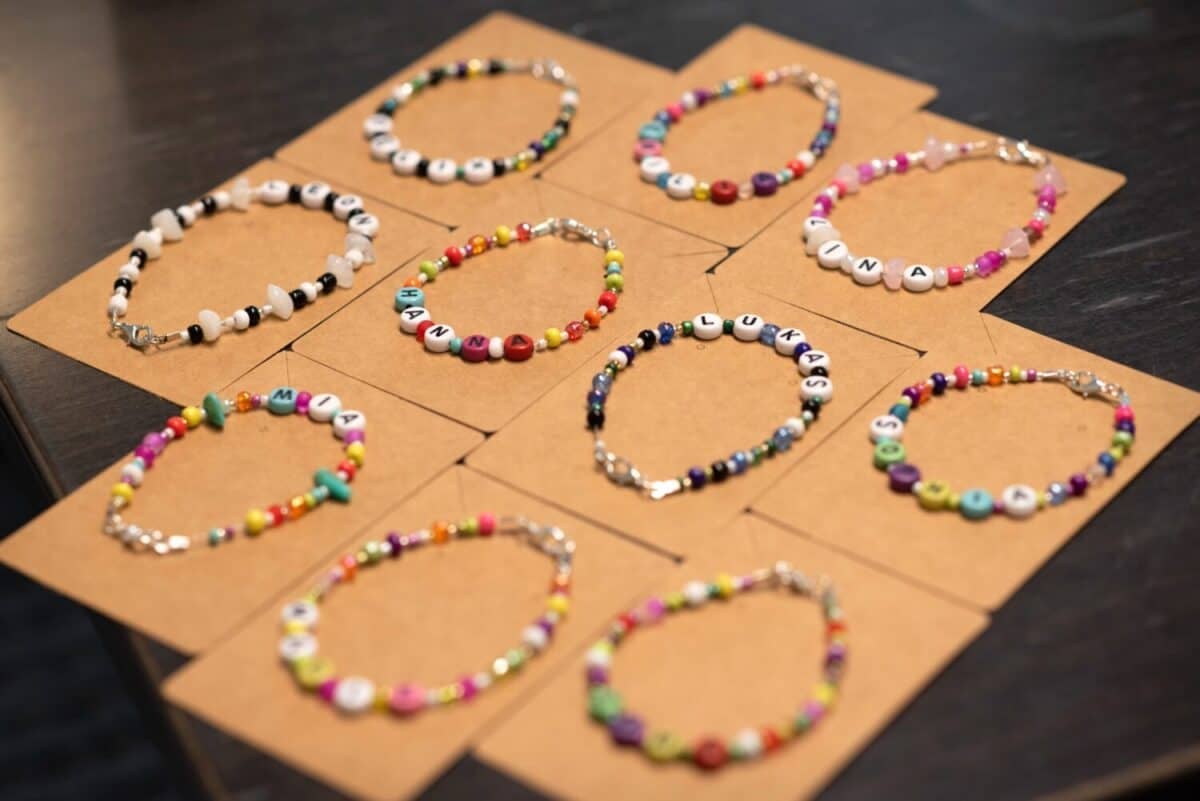 Colorful handmade kids’ bracelets with letter beads spelling names like Lina, Hanna, Lukas, Mia. Displayed on cardboard cards, ready for gift packaging.