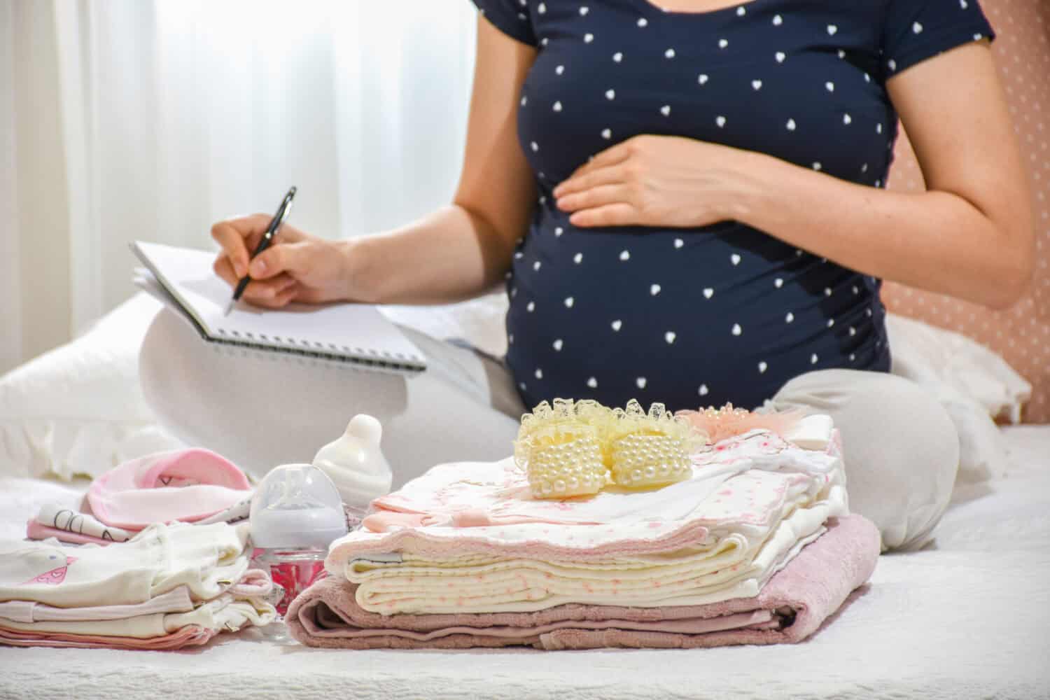 Pregnant woman is packing baby clothes for going to maternity hospital. Woman taking notes