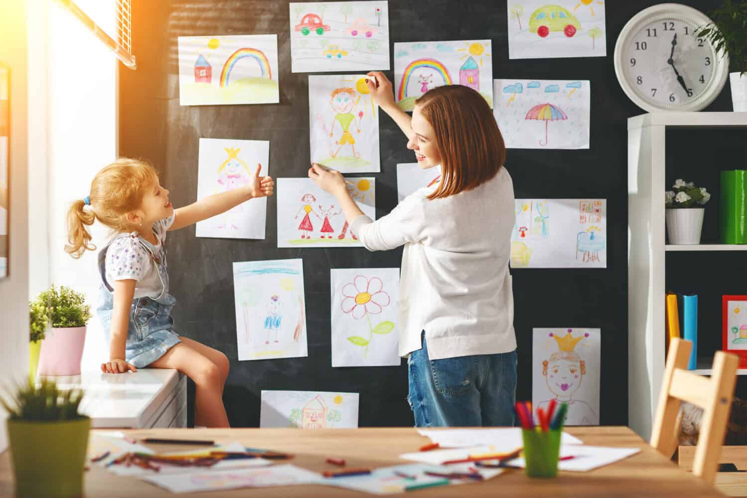 Mother and child girl hang their drawings on the wall