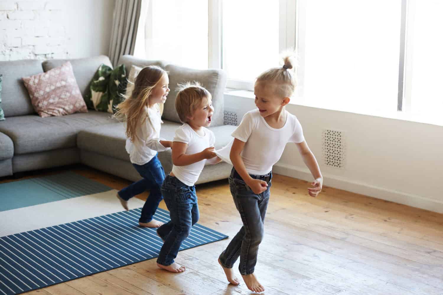 Action freeze shot of three happy joyful children one girl and two boys pullin each other by clothes while doing conga line, screaming in joy and excitement. Happiness, childhood and leisure