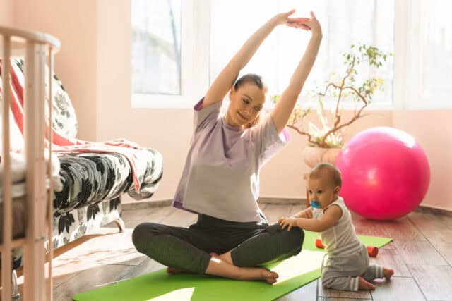 Young happy mother is practicing fitness and yoga with her little child on the sports mat at home. Self-isolation indoor sports. High quality photo