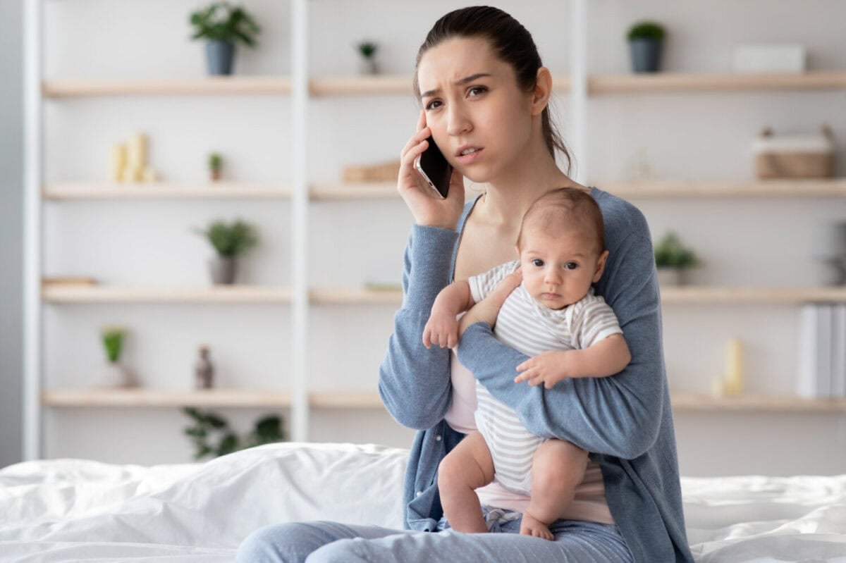 Portrait Of Worry Young Mother Holding Newborn Baby On Hands And Talking On Cellphone, Concerned Millennial Mom Calling To Doctor To Get Advice About Infant Health And Child Care, Free Space
