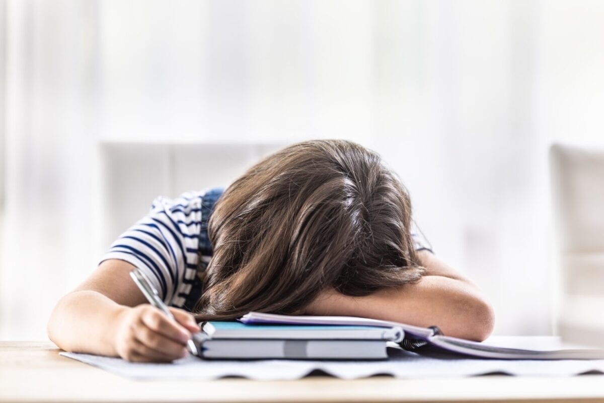 Desperate girl student has her head fallen on her arm during making homework at home.