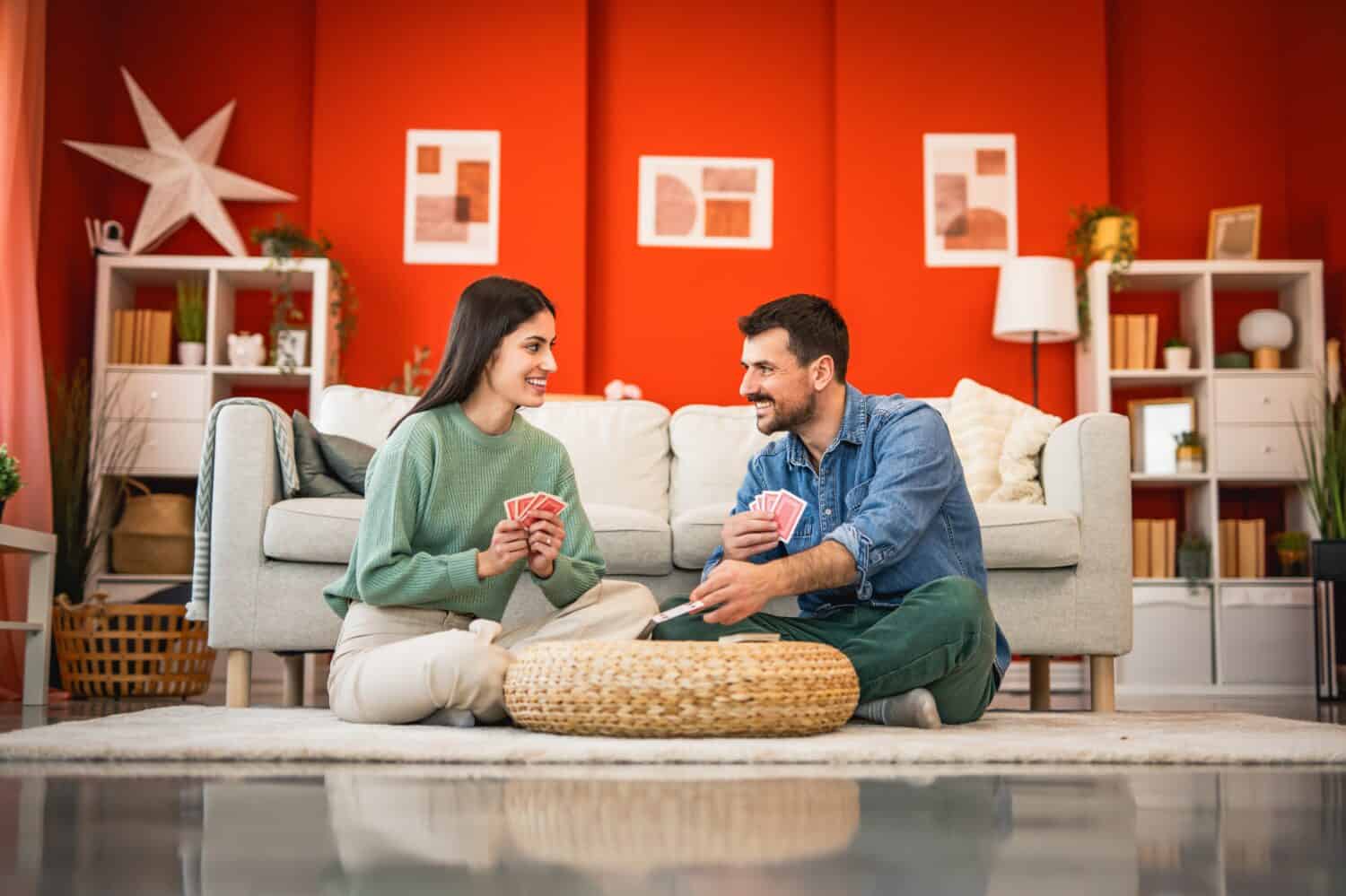 Cheerful boyfriend and girlfriend sit on floor and play cards home