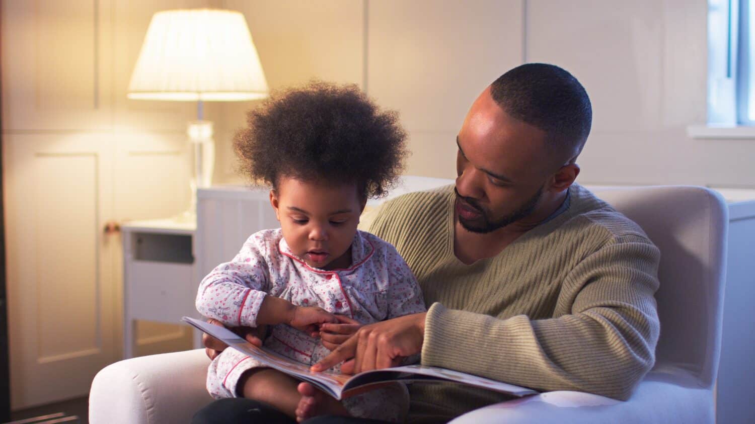Father Reading Book To Young Son Wearing Pyjamas At Home In Nursery At Bedtime
