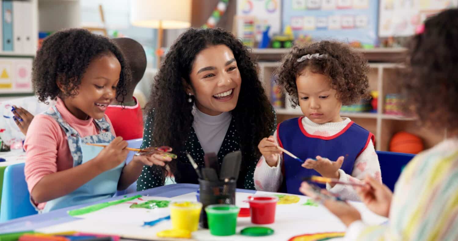 Education, kids and teacher painting hands for art, creative talent and motor skill development in preschool class. Learning, students drawing and happy children in lesson with watercolor with brush