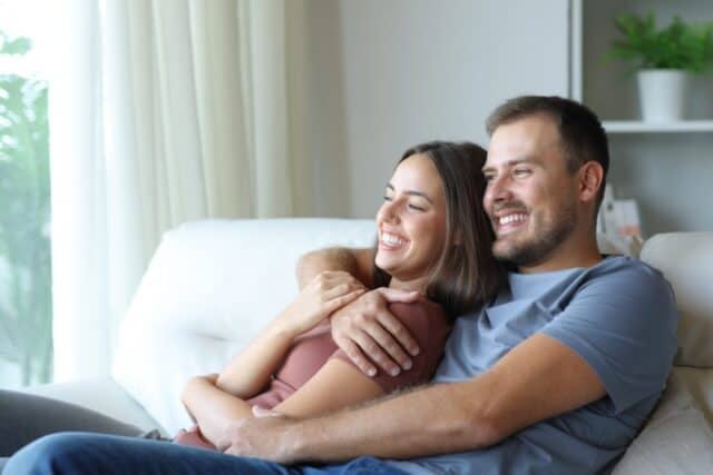 Happy couple hugging and relaxing sitting in a couch at home
