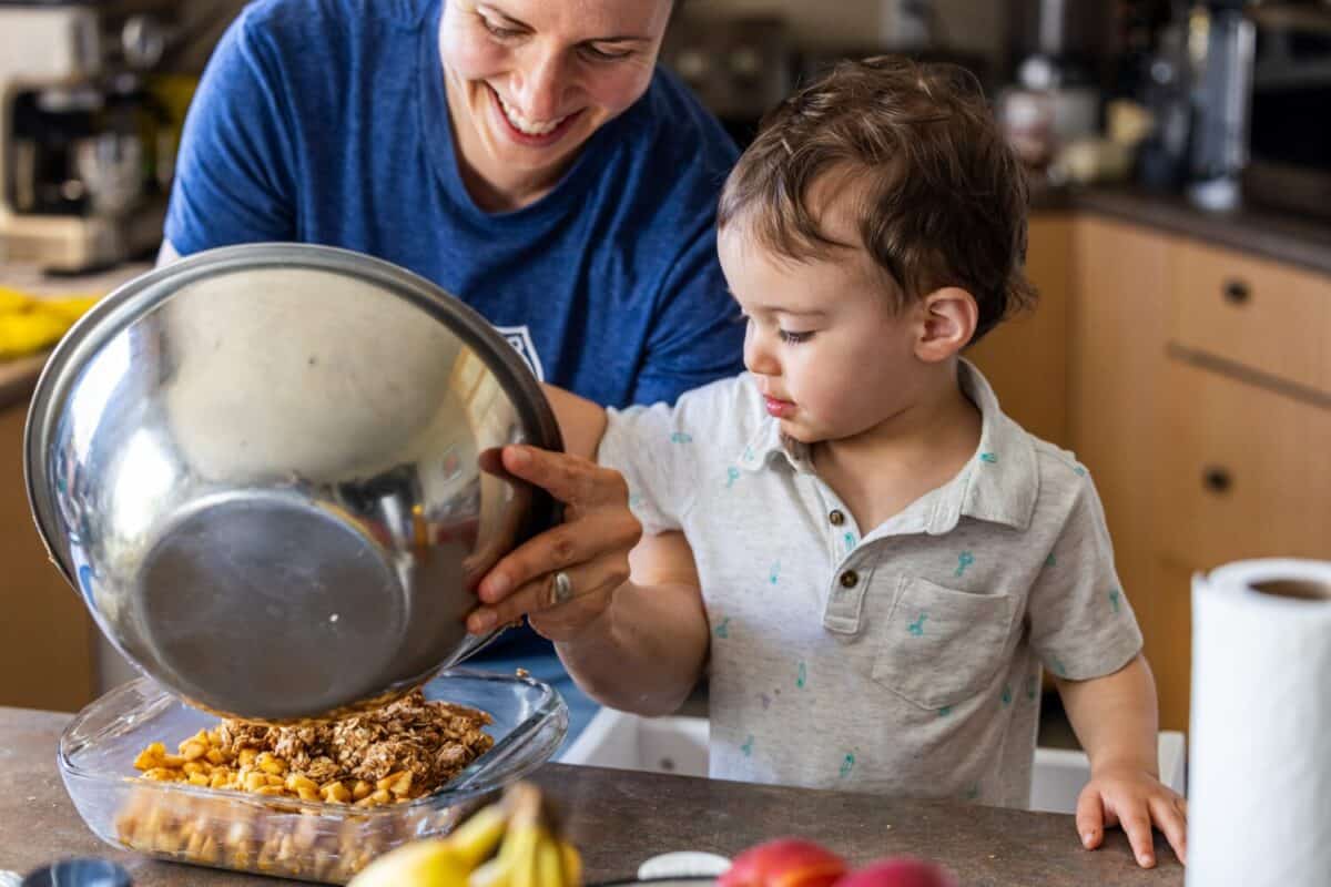 Joyful boy toddler cooking in kitchen with parent's assistance in preparation.
