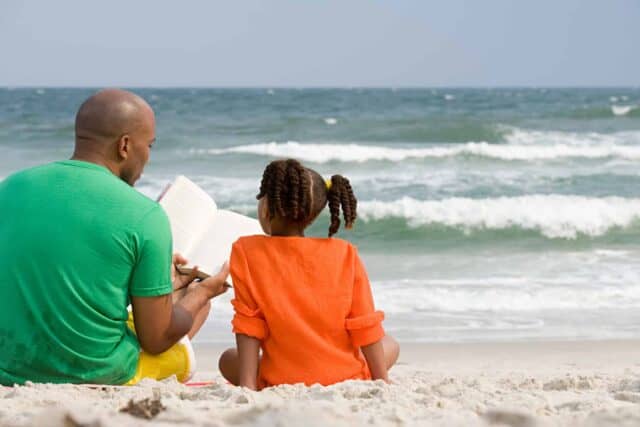 dad reading to daughter near ocean