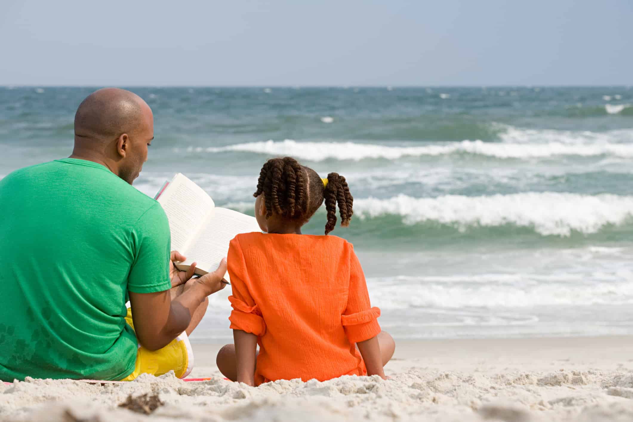 dad reading to daughter near ocean