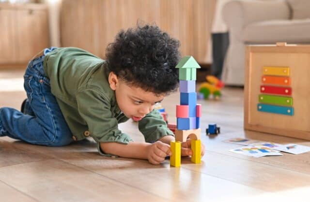 Concentrated latinos boy playing toys sitting on warm floor in modern living room. Baby development. Small tower. Learning creative concept