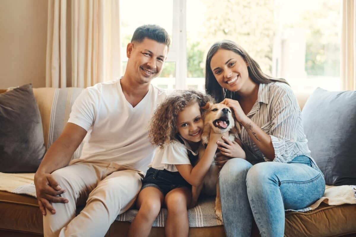 Mother, father and girl with dog for portrait on sofa for love, bonding and affection with safety or animal. Mom, dad and kid with family pet in home with care, together and relax with happiness.