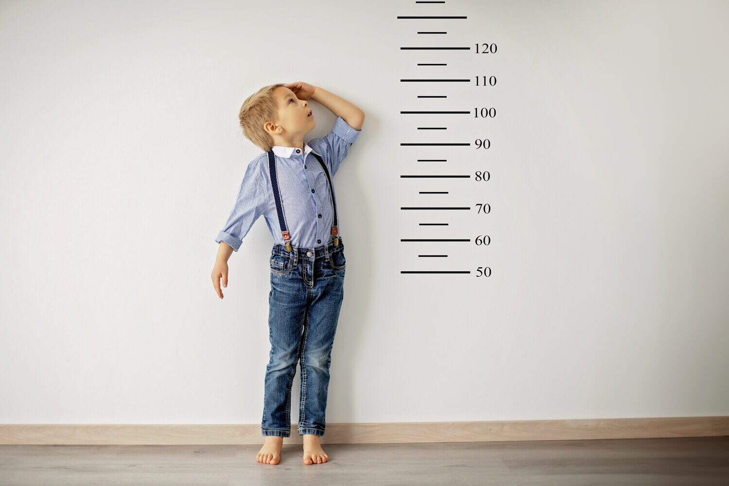 Little child, blond boy, measuring height against wall in room
