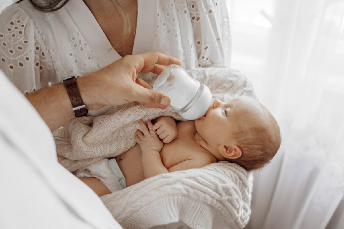 A man is feeding a baby with a bottle. The baby is lying on a blanket and the bottle is in the man's hand. Concept of warmth and care as the man feeds the baby