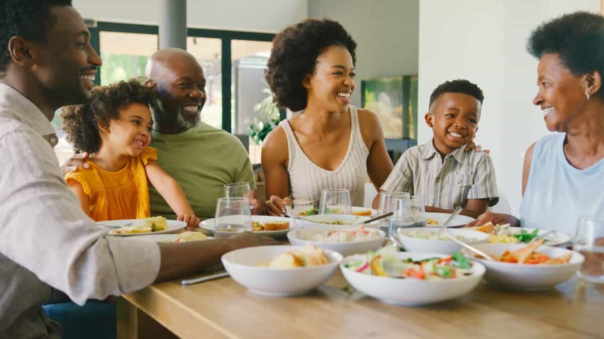 Multi-Generation Family Sitting Around Table Eating Meal At Home Together