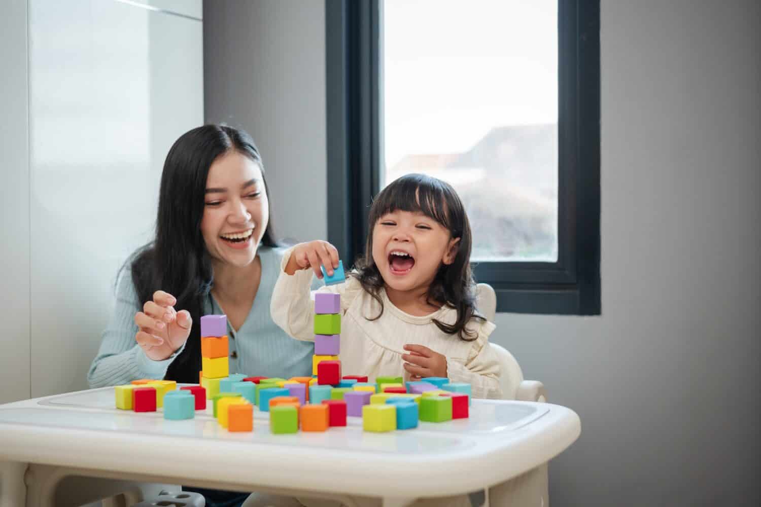 happy toddler girl playing wooden block toy cubes with her mother on a table