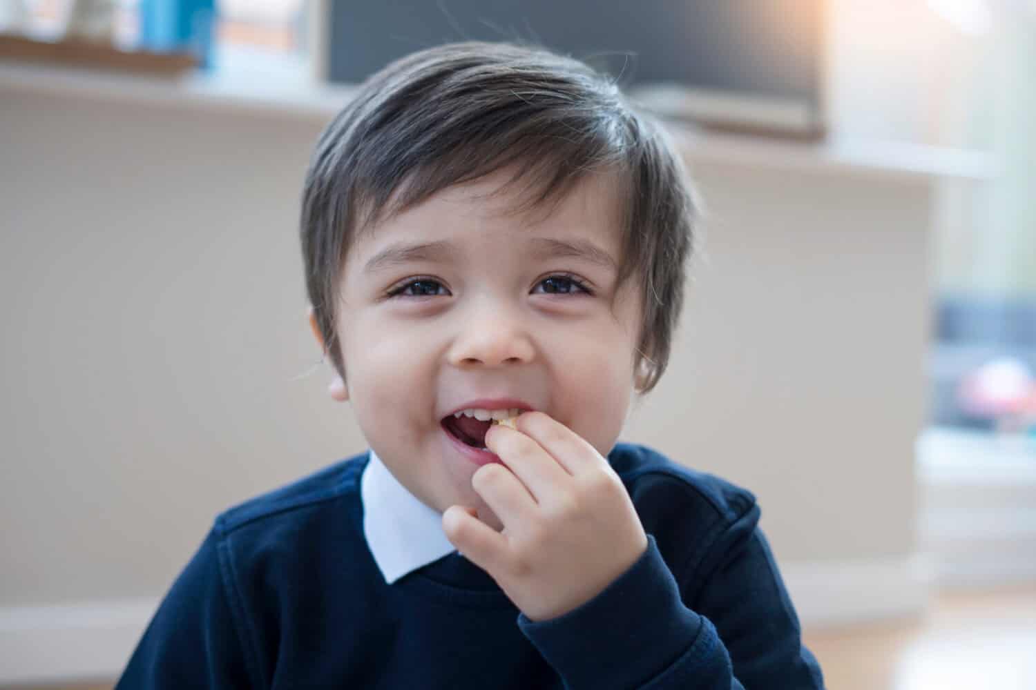 Active little boy enjoy eating popcorn, Little boy wearing school uniform sitting and eating pop corn for his snack at home after back from school, Children food or snack concept