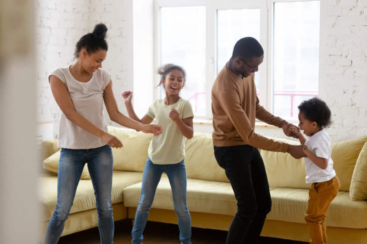 Happy african american mother and father with two children dancing. Diverse brother and sister with parents enjoying tender moment at living room.