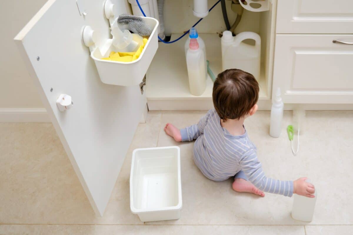 A child is playing with chemical cleaning products under the sink in the kitchen. Baby holds bottles with detergent. Kid aged about two years (one year nine months)