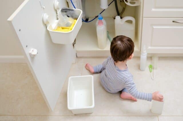A child is playing with chemical cleaning products under the sink in the kitchen. Baby holds bottles with detergent. Kid aged about two years (one year nine months)