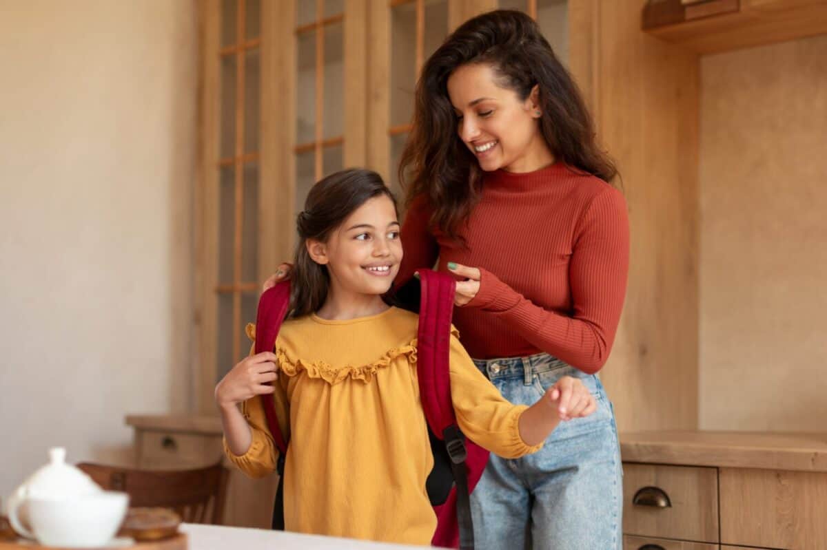 Young Arabic Mom Putting Backpack On Daughter's Shoulders Sending Her To School, Preparing Preteen Schoolgirl Kid For Classes At Modern Home Interior. Morning Preparation, Schooler Gets Ready