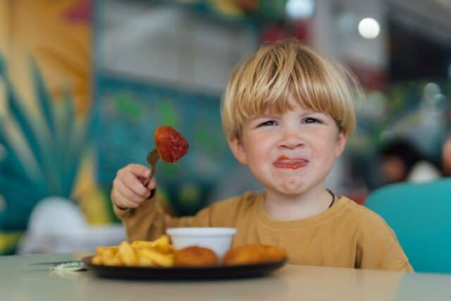 happy boy with blond hair eats fries and nuggets in restaurant