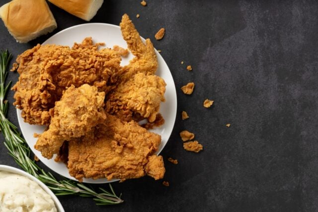 A platter of fried chicken with mashed potatoes, dinner rolls and sprig of thyme. Shot overhead on a slate background with copy space.