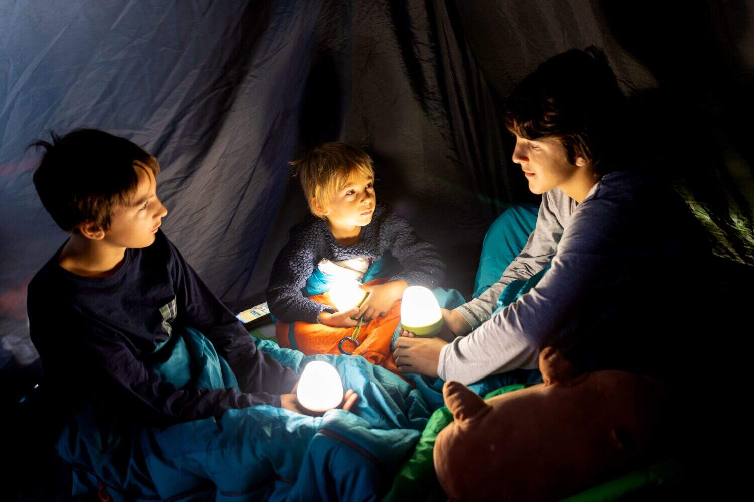 Children, boys siblings, enjoying a night in a tent in camping, laughing and reading books