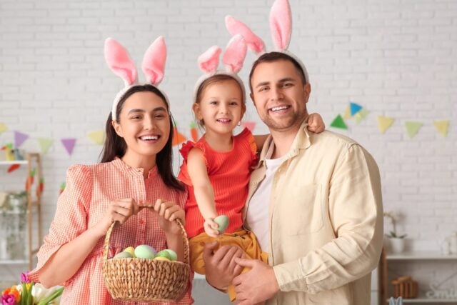 Happy family in bunny ears holding basket with Easter eggs at home