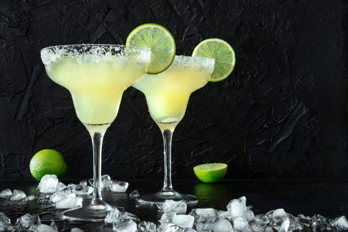 Margarita cocktail in the classic glasses, side view on a black background, with ice. Summer drinks with lime and a salt rim, with copy space