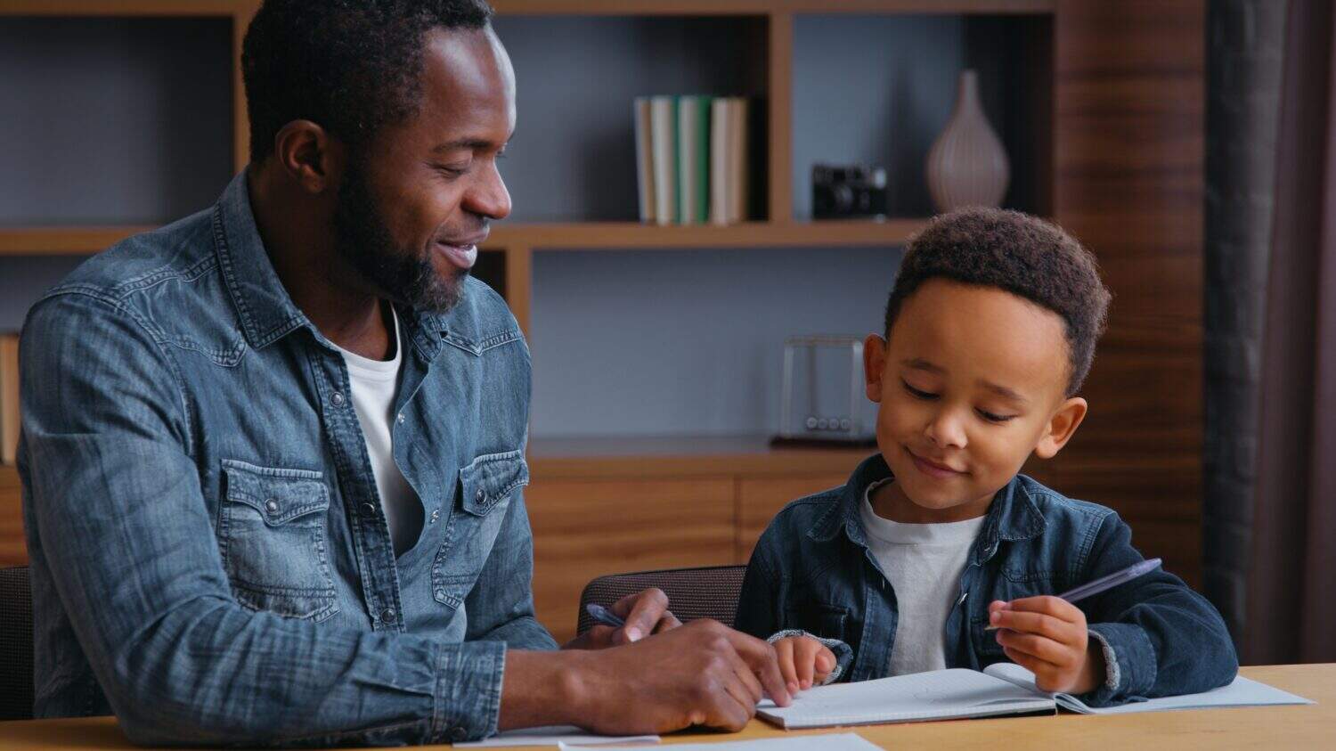 African American family clever father help son writing letters write homework man teacher tutor teaching little ethnic boy kid child pupil preparing to school dad distant busy elementary education