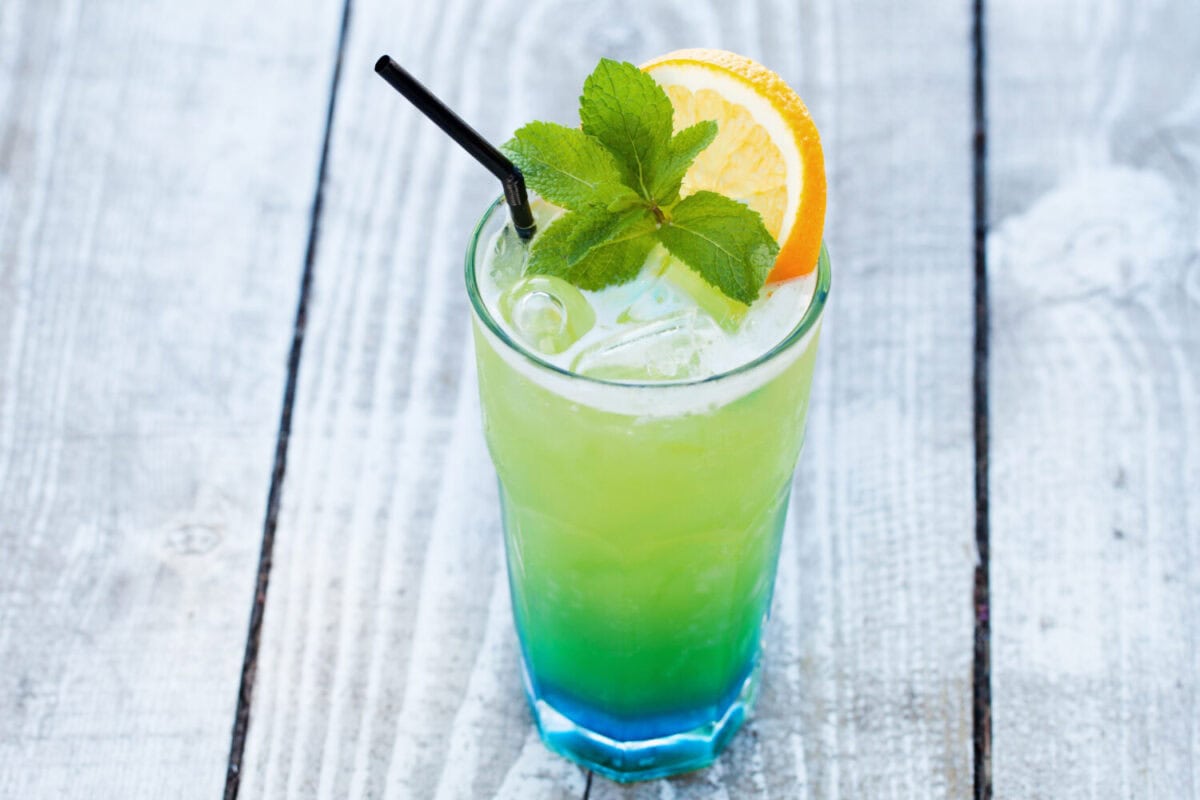 blue green cocktail with orange and mint on a wooden table
