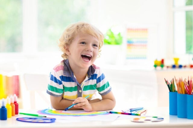 Kids paint. Child painting in white sunny study room. Little boy drawing rainbow. School kid doing art homework. Arts and crafts for kids. Paint on children hands. Creative little artist at work.