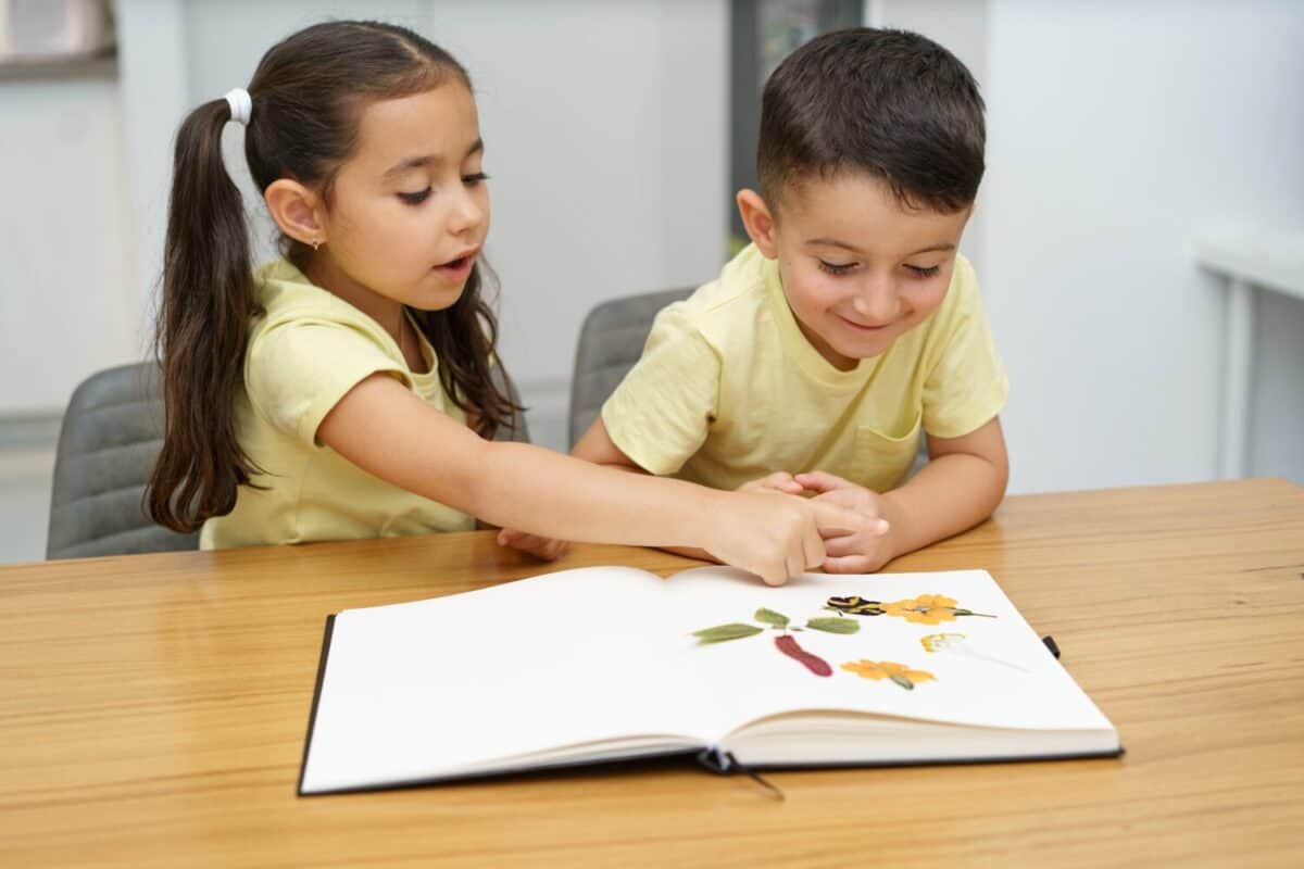 Children making herbarium. Funny kids arranging pressed flowers in a book.