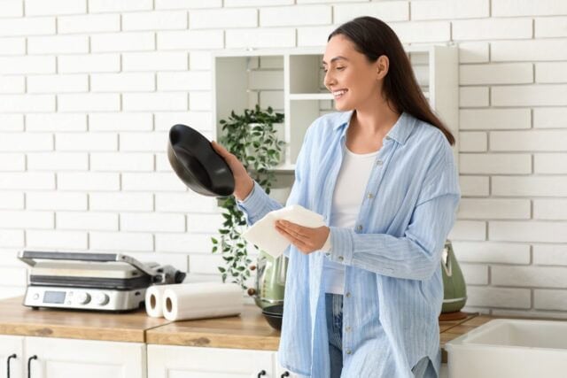 Beautiful young happy woman wiping bowl with paper towels in kitchen