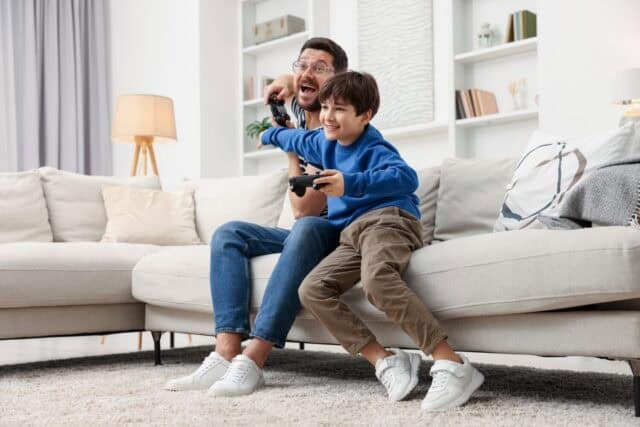 Father and his son playing video games on sofa in living room