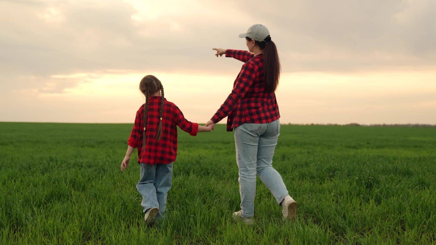 mother farmer leads child kid girl by hand through green field wheat sunset, family business, happy family sunset, agricultural family business, mother guiding child, sunset field journey, family farm
