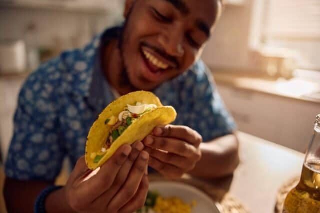 Close up of African American man eating tacos for lunch at dining table.