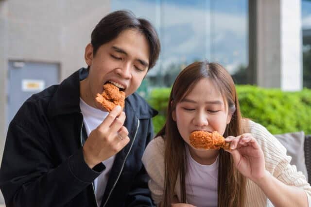Young Asian couple eating fried chicken outdoors