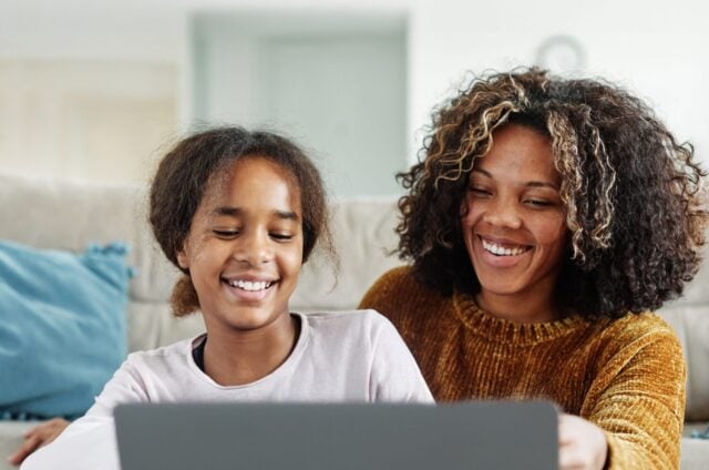 Mother and daughter doing homework with laptop at home. Mom, dad and teenage black girl happy using laptop. Teen girl and parents sitting at home working with notebook
