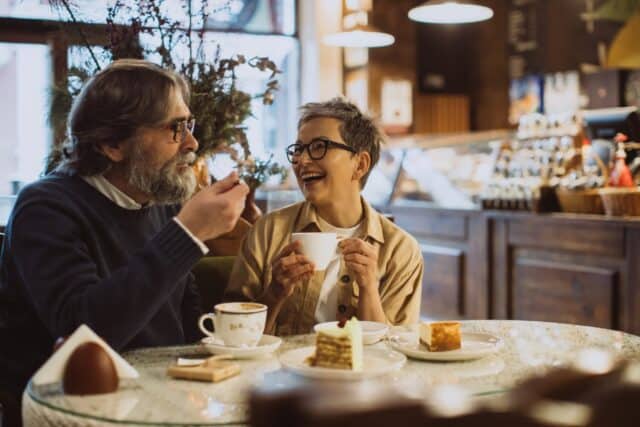 Happy mature couple relaxing at a cafe, drinking coffee and eating cake. Sharing a joyful moment together on a date