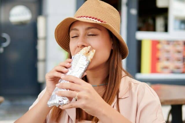 A Hispanic woman eating a burrito in an open-air restaurant