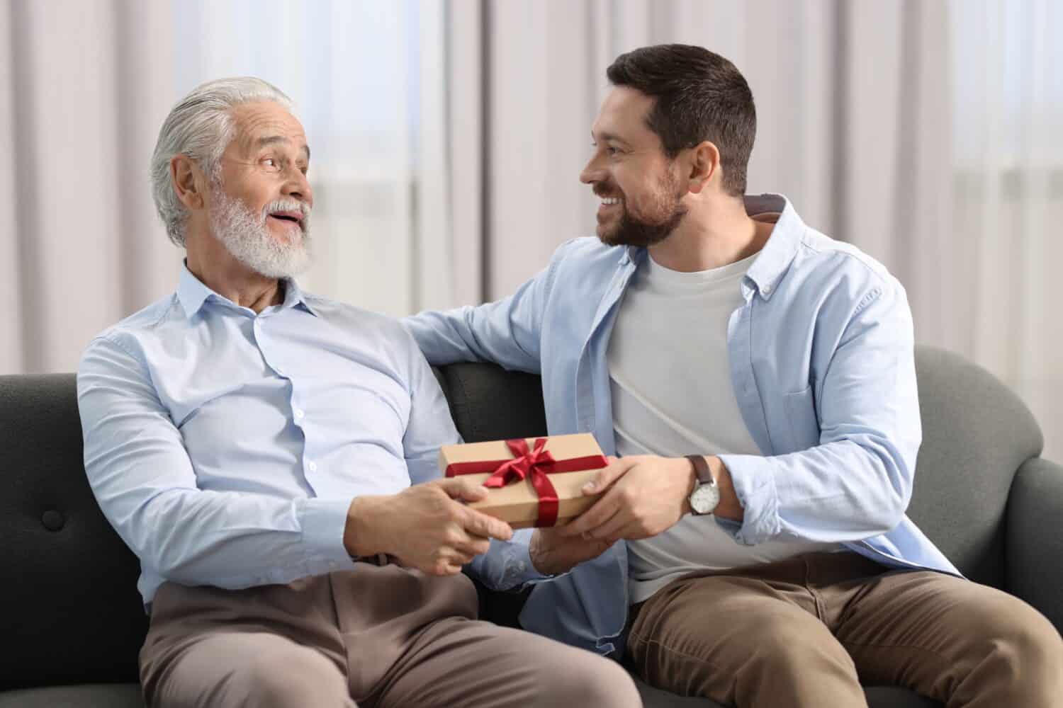 Son giving gift box to his dad on sofa at home