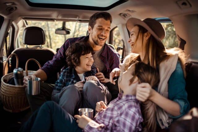 Family enjoying a road trip inside their car with kids taking photos and drinking from thermos