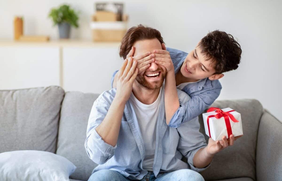 Happy father's day. Son congratulating his daddy, covering his eyes from behind, greeting and giving present at home. Family holiday celebration, surprise present for dad