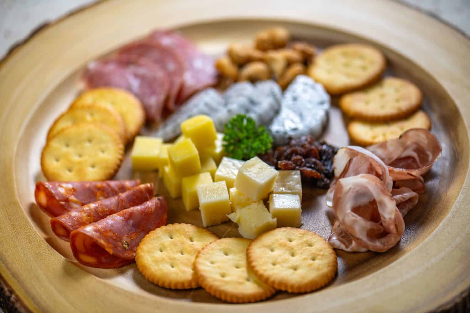 Plate of assorted meats and cheeses with crackers. The crackers are arranged in a circle around the meats and cheeses