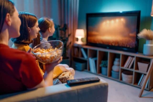 Happy family spending time together. Mother and children watching TV, movies with popcorn in the evening at home.