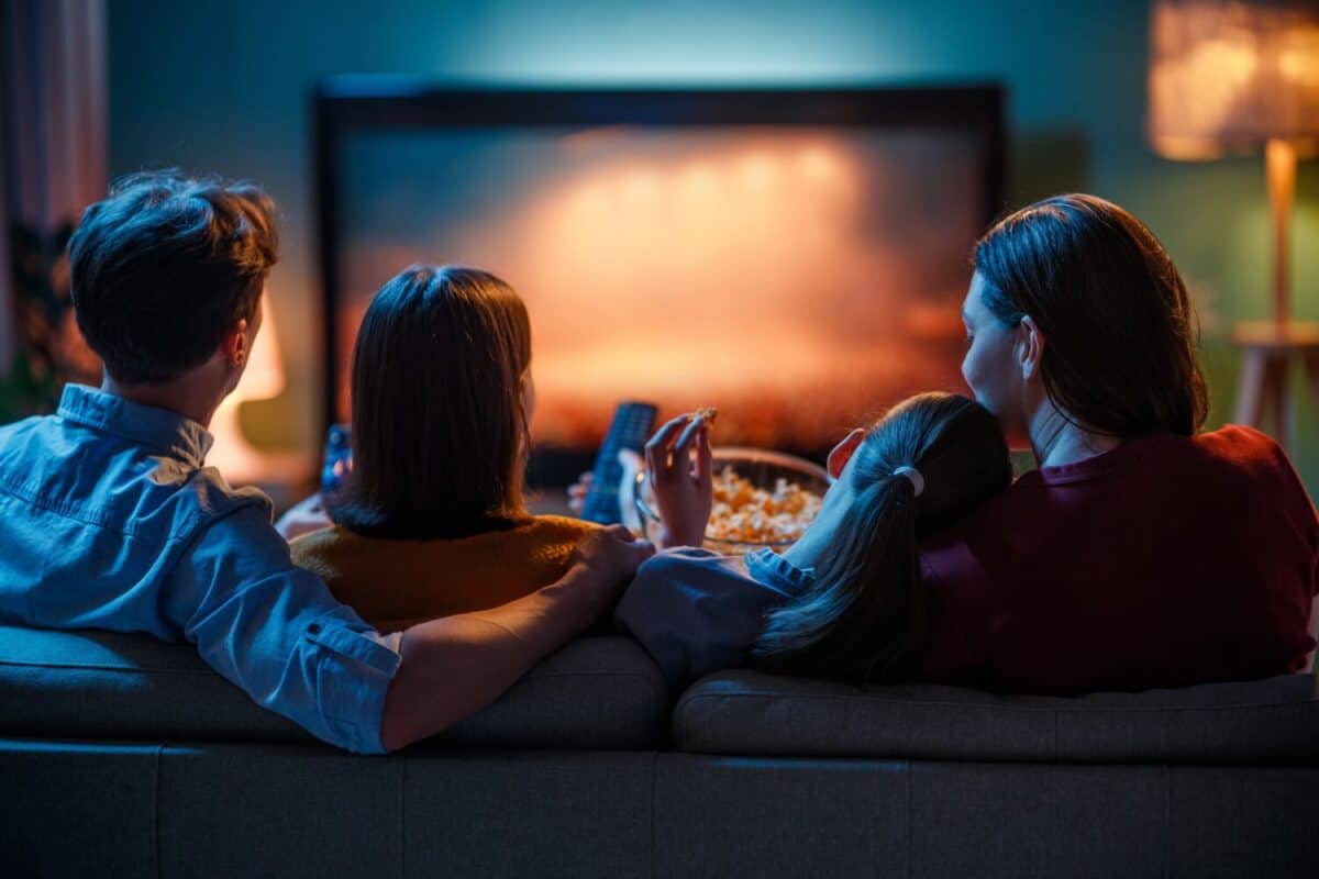 Happy family spending time together. Mother, father and children watching TV, movies with popcorn in the evening at home.